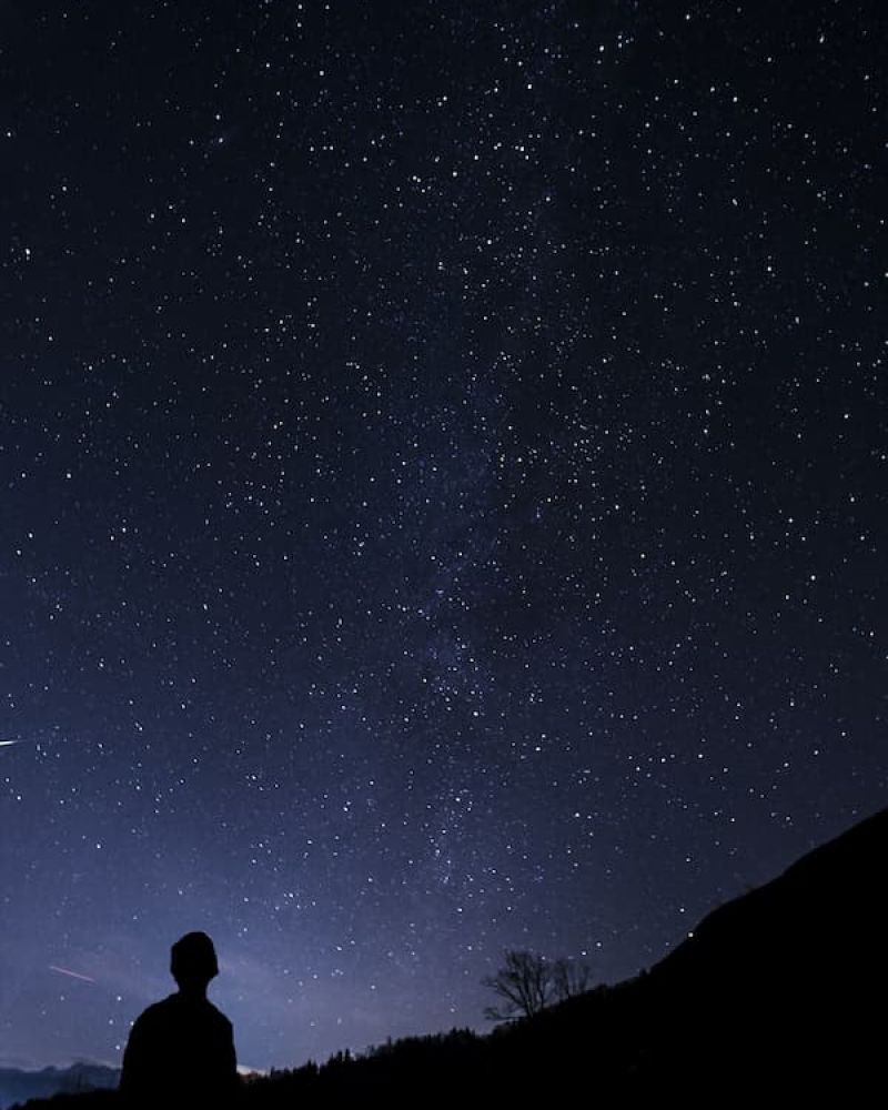 Silhouetted figure gazing up at the Milky Way and stars over a dark hillside