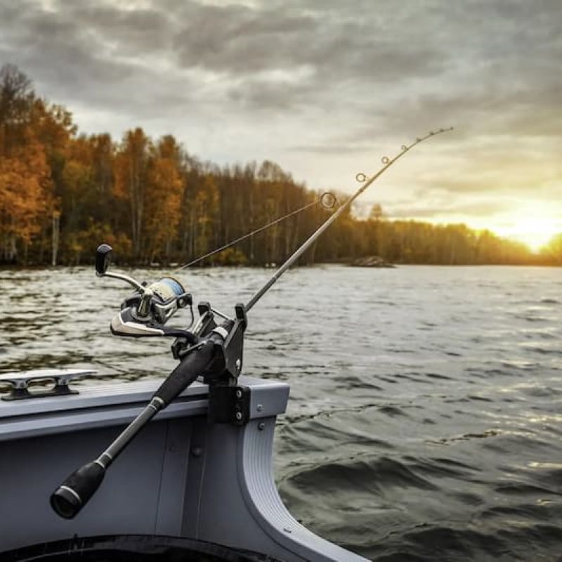 Fishing rod mounted on boat bow over a lake at autumn sunset