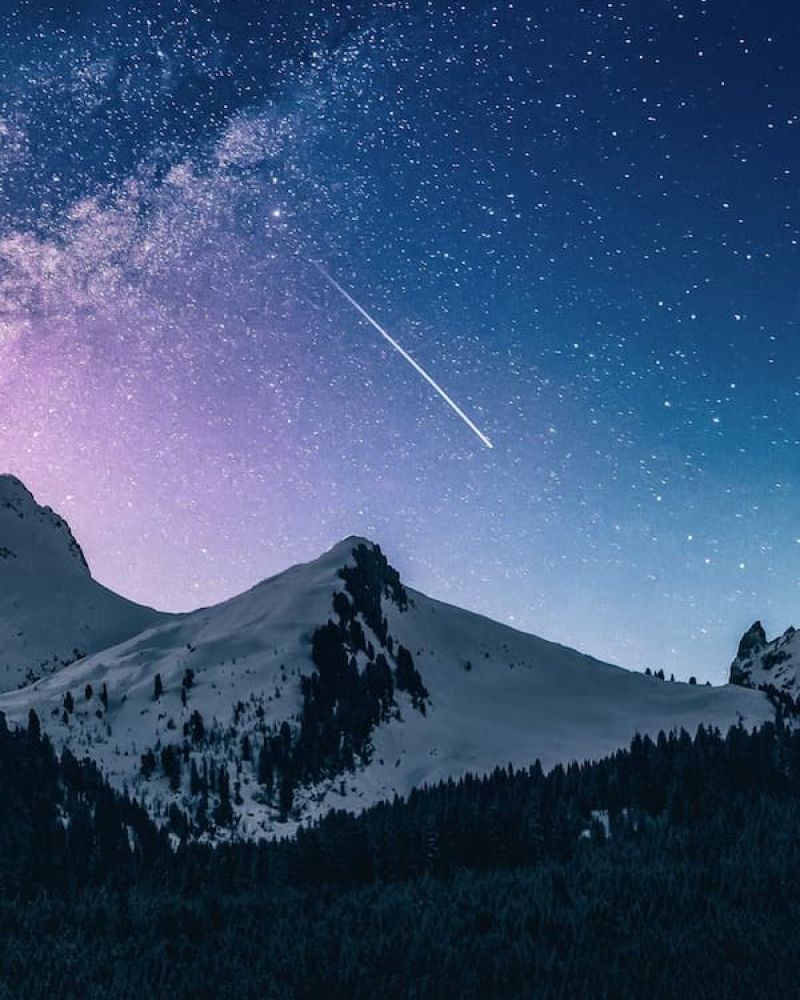 Shooting star streaking across a starry night sky above snow-covered mountain peaks
