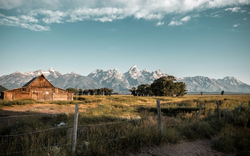 Old wooden barn on a grassy plain with the Teton mountain range in background