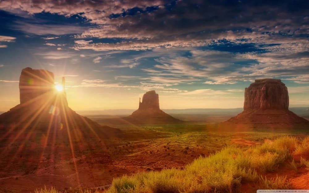 Desert mesas at sunrise with sunburst over red rock formations