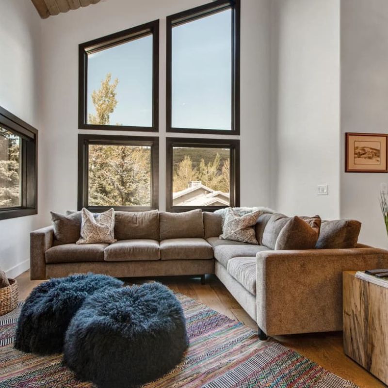 Bright living room with sectional sofa and tall windows facing trees