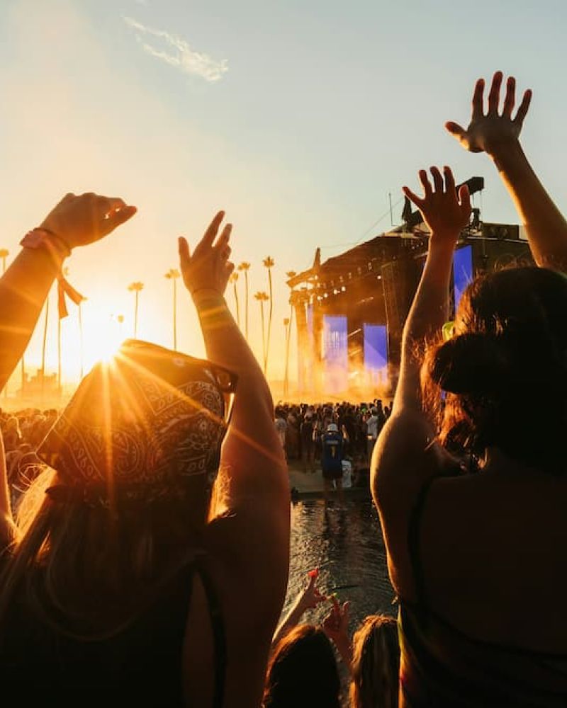 Concertgoers raising hands at an outdoor music festival stage at sunset