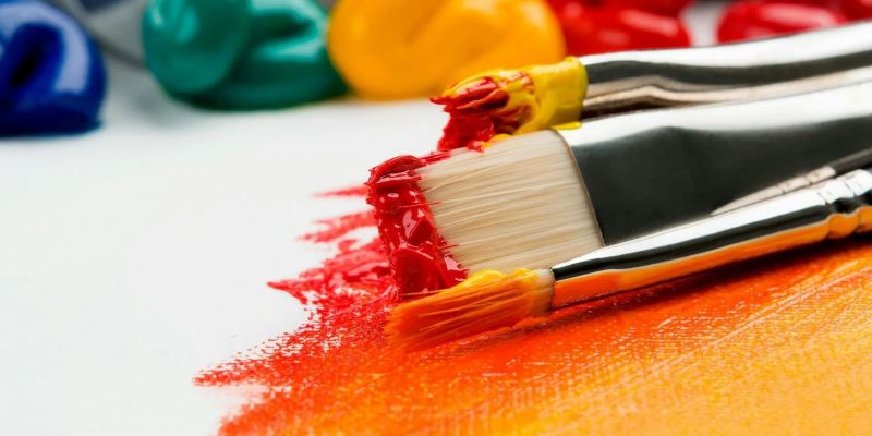 Paintbrushes loaded with red and yellow paint on a canvas
