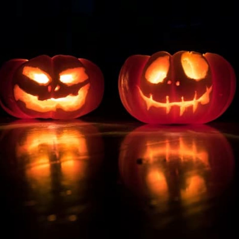 Two carved jack-o-lanterns glowing on a dark reflective surface
