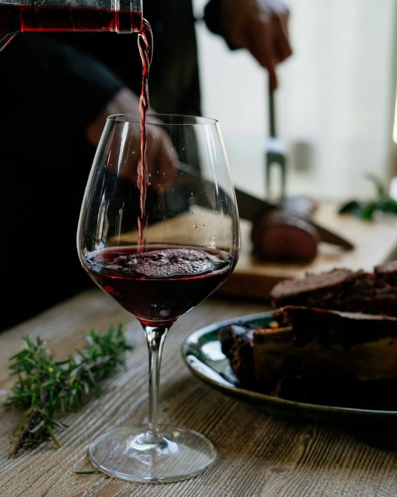 Red wine being poured into a glass beside a chocolate dessert and herbs