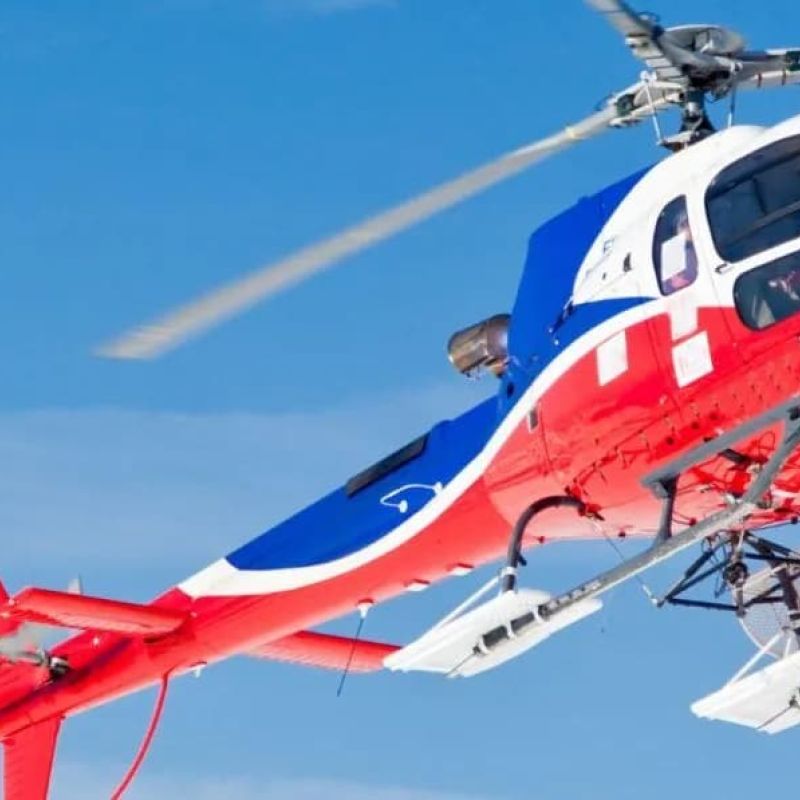 Red and blue helicopter banking above snow-covered mountain peaks