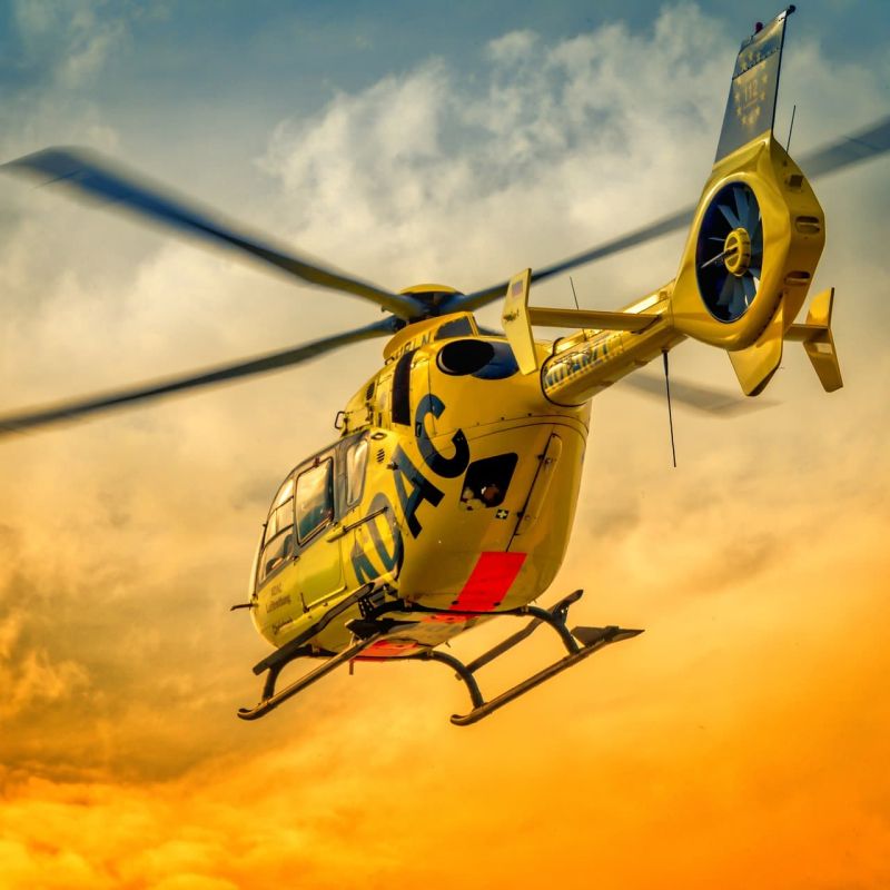 Yellow rescue helicopter in flight against an orange sunset sky