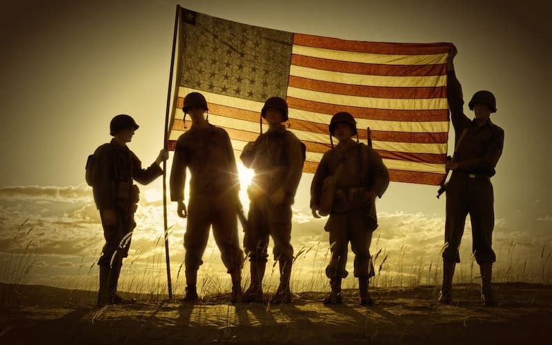 Silhouetted soldiers holding an American flag at sunset