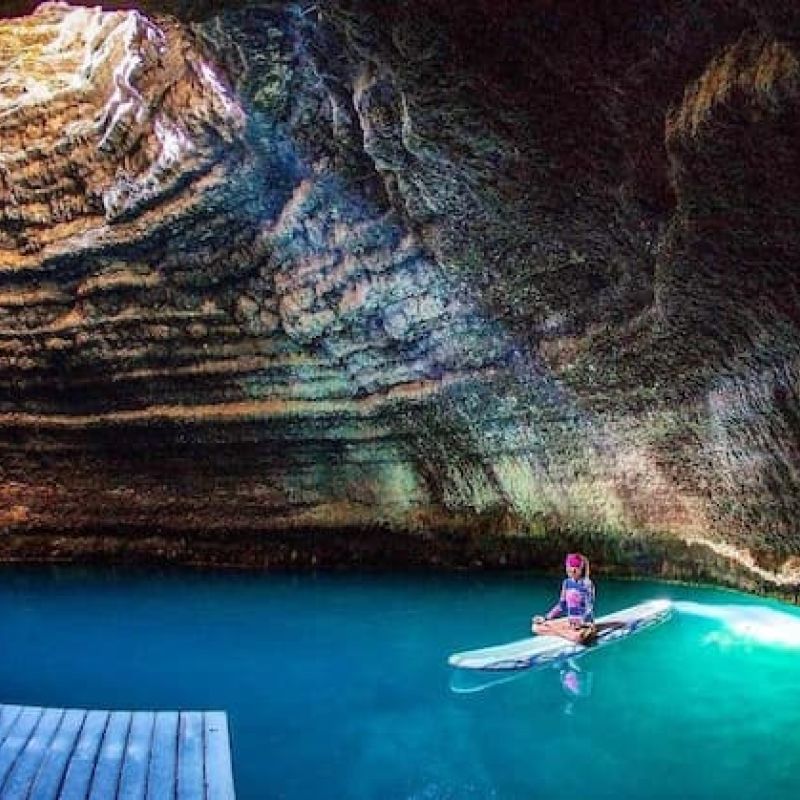 Paddleboarder on turquoise water inside a sandstone cavern at Homestead Crater
