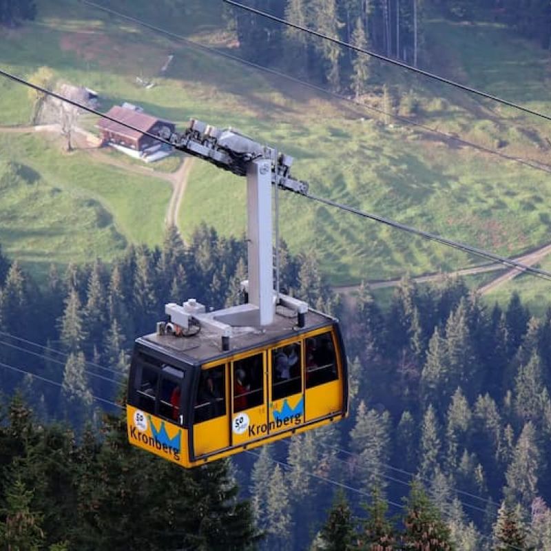 Yellow Kronberg cable-car gondola crossing above green alpine forest