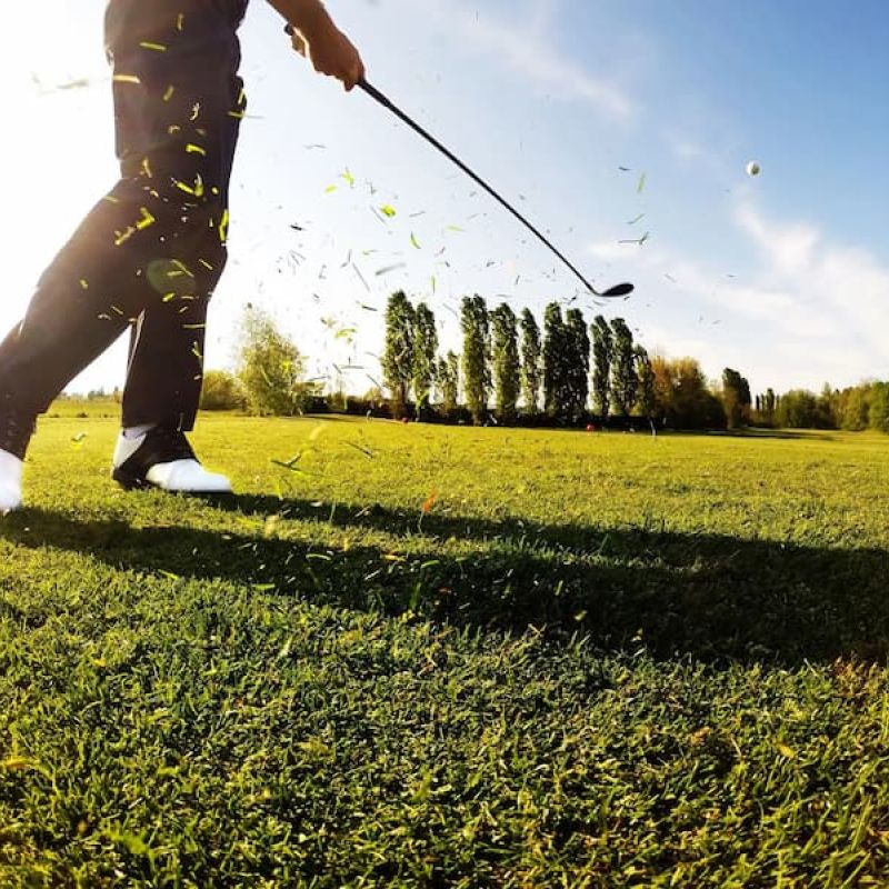 Golfer mid-swing on a tee box with grass clippings flying