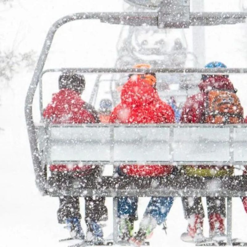 Skiers riding a chairlift through heavy falling snow on the mountain