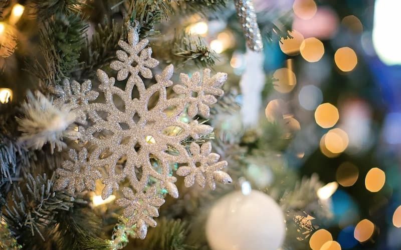 Silver snowflake ornament hanging on a lit Christmas tree