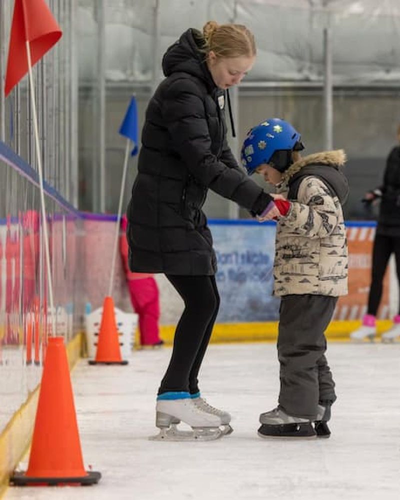 Instructor helping a young child learn to ice skate at an indoor rink