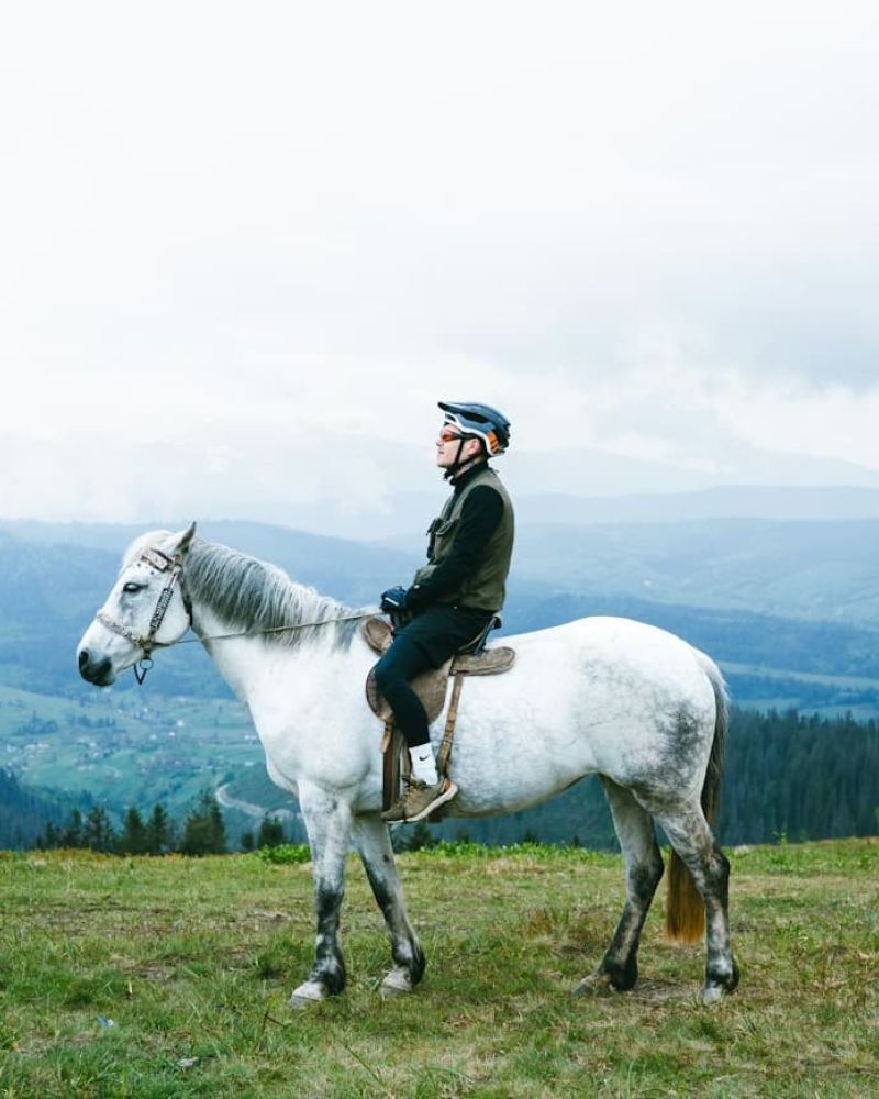 Helmeted rider on a white horse atop a mountain ridge