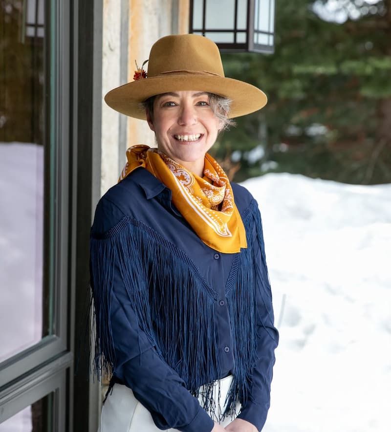 Smiling woman in brown felt hat and fringed navy shirt with orange scarf