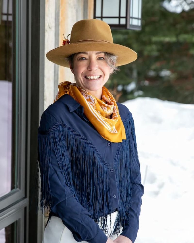 Smiling woman in brown felt hat and fringed navy shirt with orange scarf