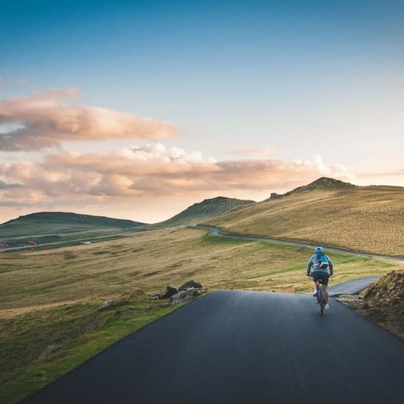 Cyclist riding a paved road through open rolling hills at dusk