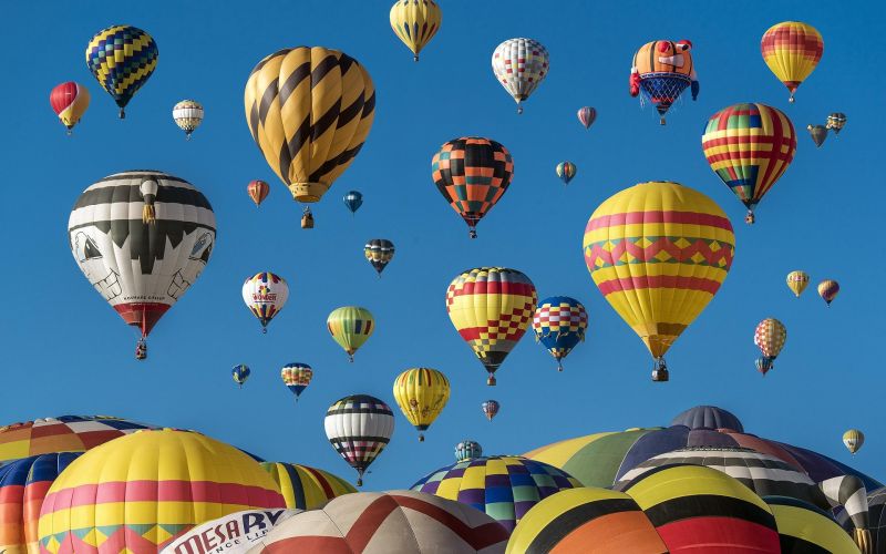 Colorful hot air balloons rising into a clear blue sky at a balloon festival