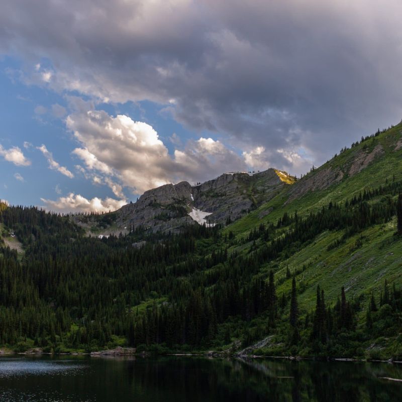Forested mountain ridge above an alpine lake under partly cloudy sky