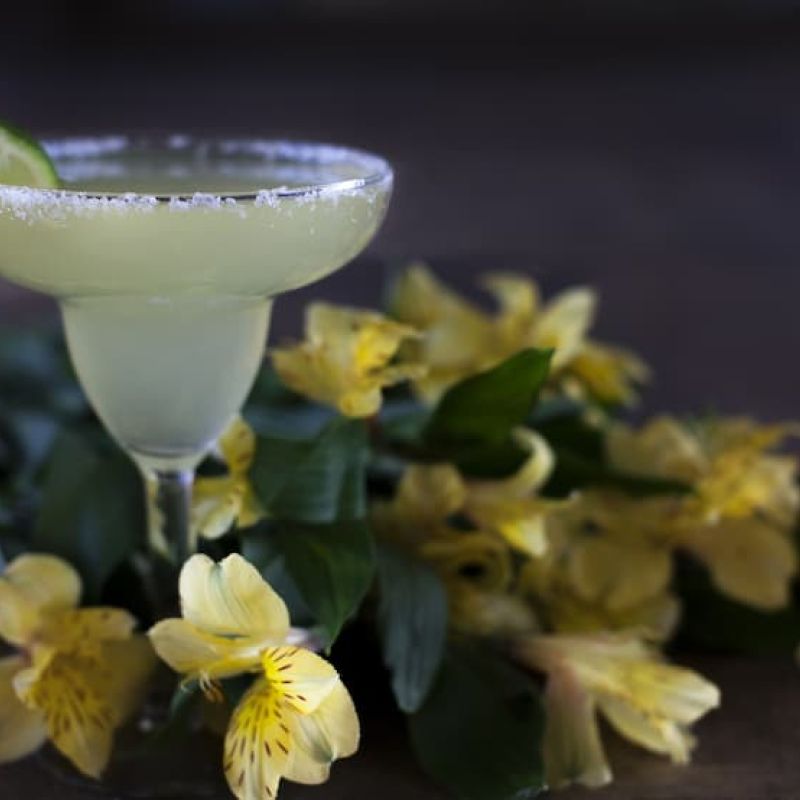 Margarita with salted rim and lime wedge beside yellow alstroemeria flowers