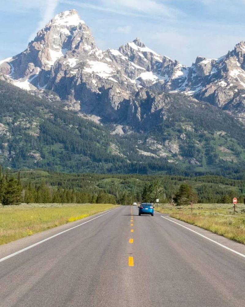 Open highway leading toward the jagged Grand Teton range under a bright sky