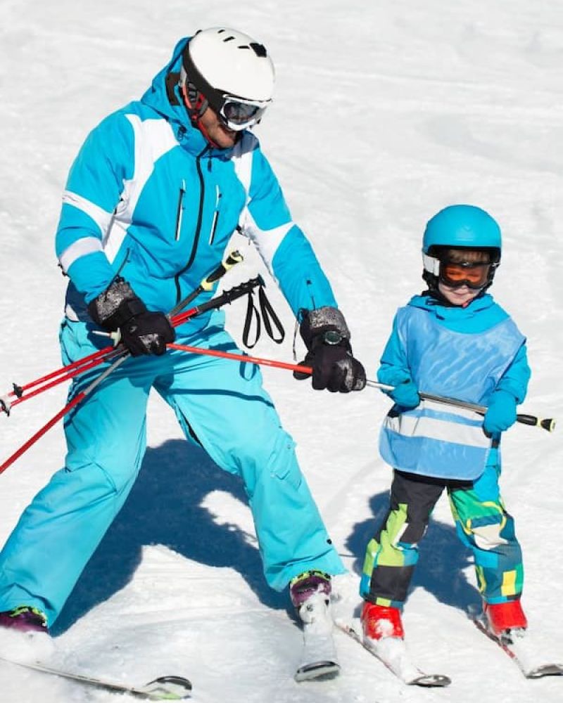 Ski instructor guiding a young child on skis at a beginner slope