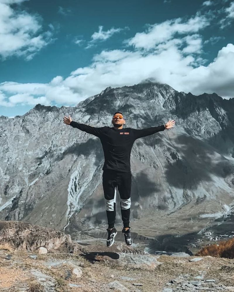 Person leaping with arms outstretched on a ridge before rugged mountains
