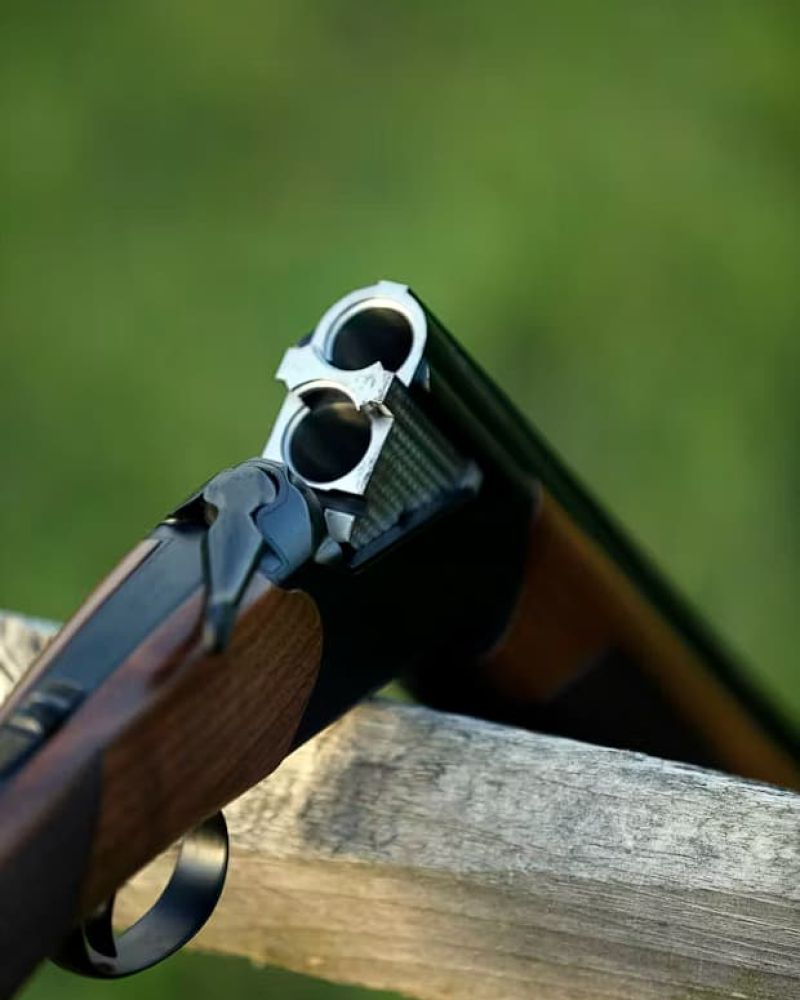Open over-under shotgun resting on a wooden fence rail