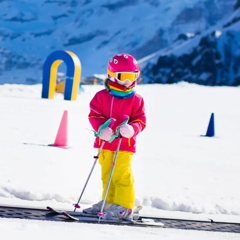 Young child in pink jacket learning to ski on a magic carpet lift