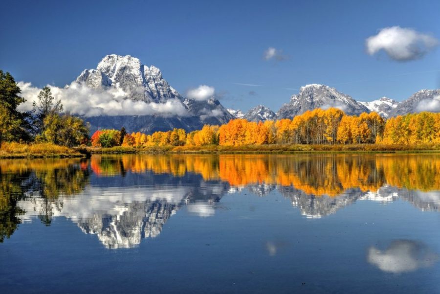 Snow-dusted Teton peaks reflected in a still lake bordered by golden aspens