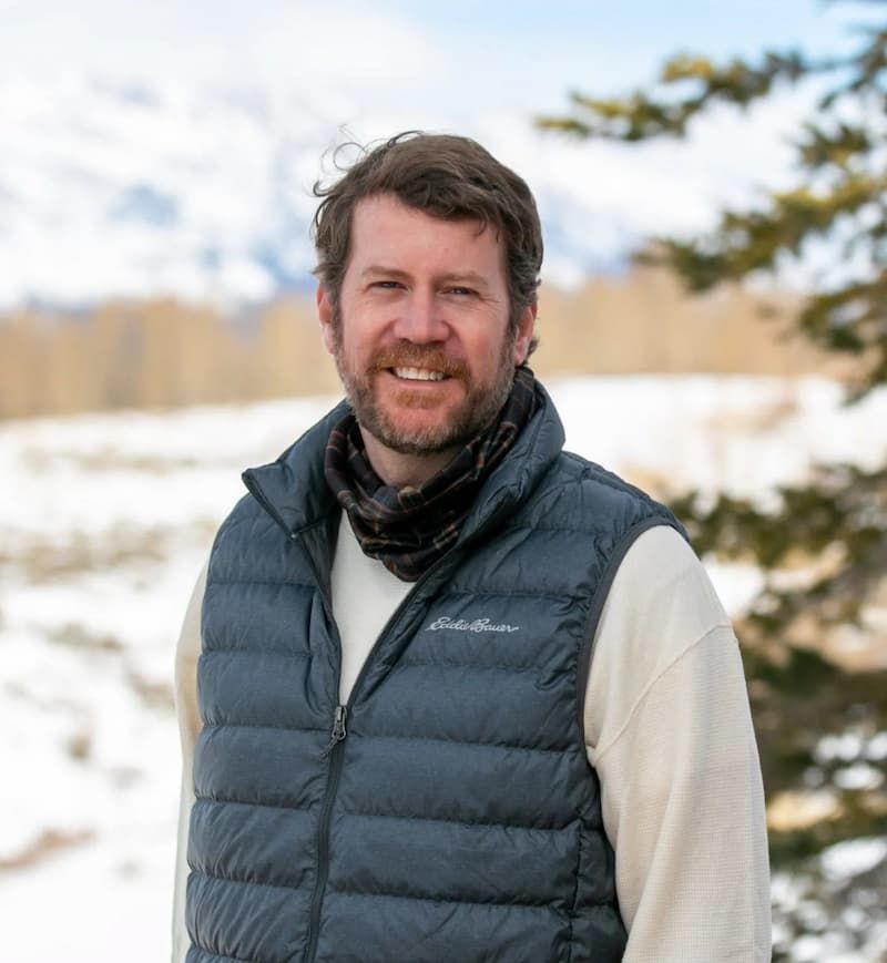 Bearded man in gray Eddie Bauer vest smiling in a snowy mountain landscape