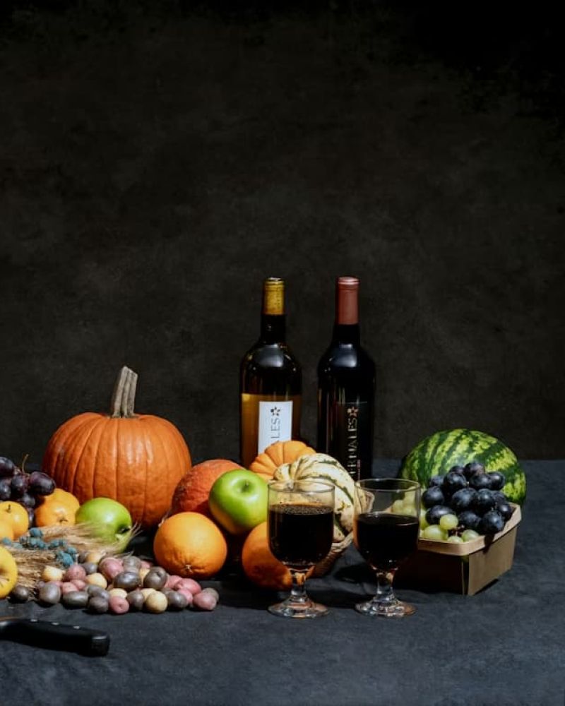 Cornucopia of fruits, pumpkin, bread, and wine arranged on a dark table