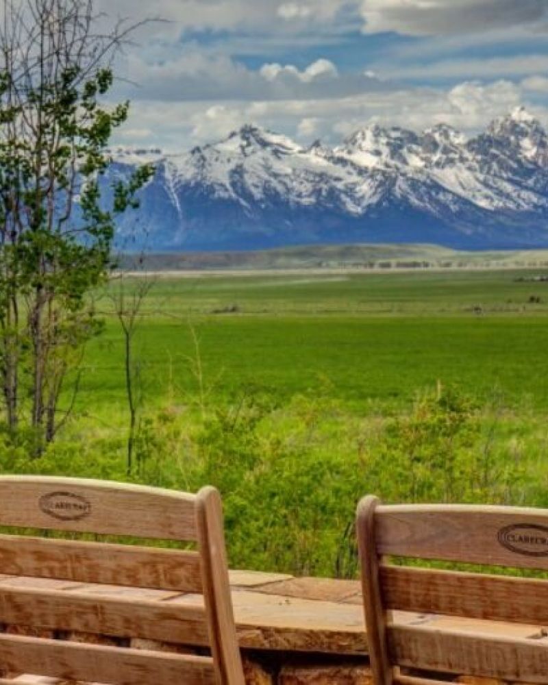 Two wooden chairs facing a meadow with the snowcapped Teton range