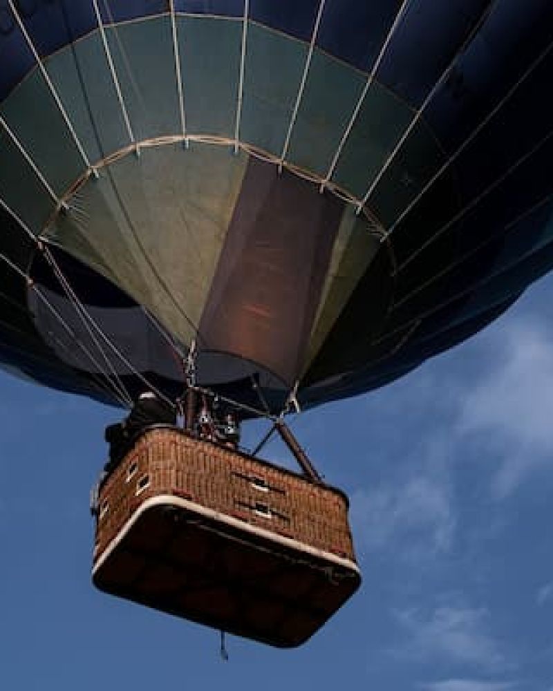 Hot air balloon basket viewed from below against a partly cloudy blue sky