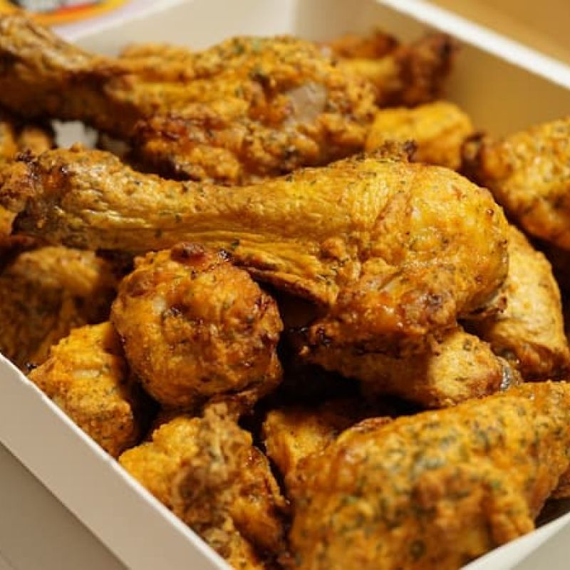 Box of seasoned fried chicken drumsticks and wings
