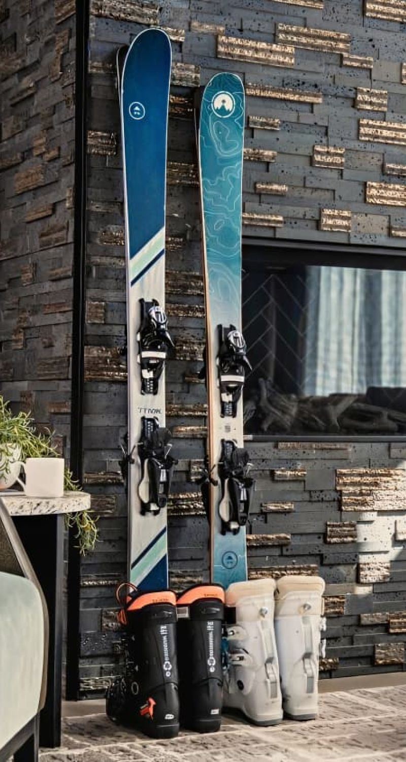 Pair of skis and ski boots staged against a stone fireplace in a living room