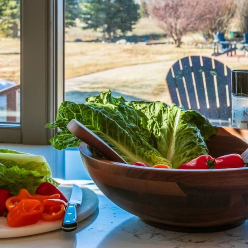 Salad bowl with romaine and peppers on a kitchen counter overlooking a meadow