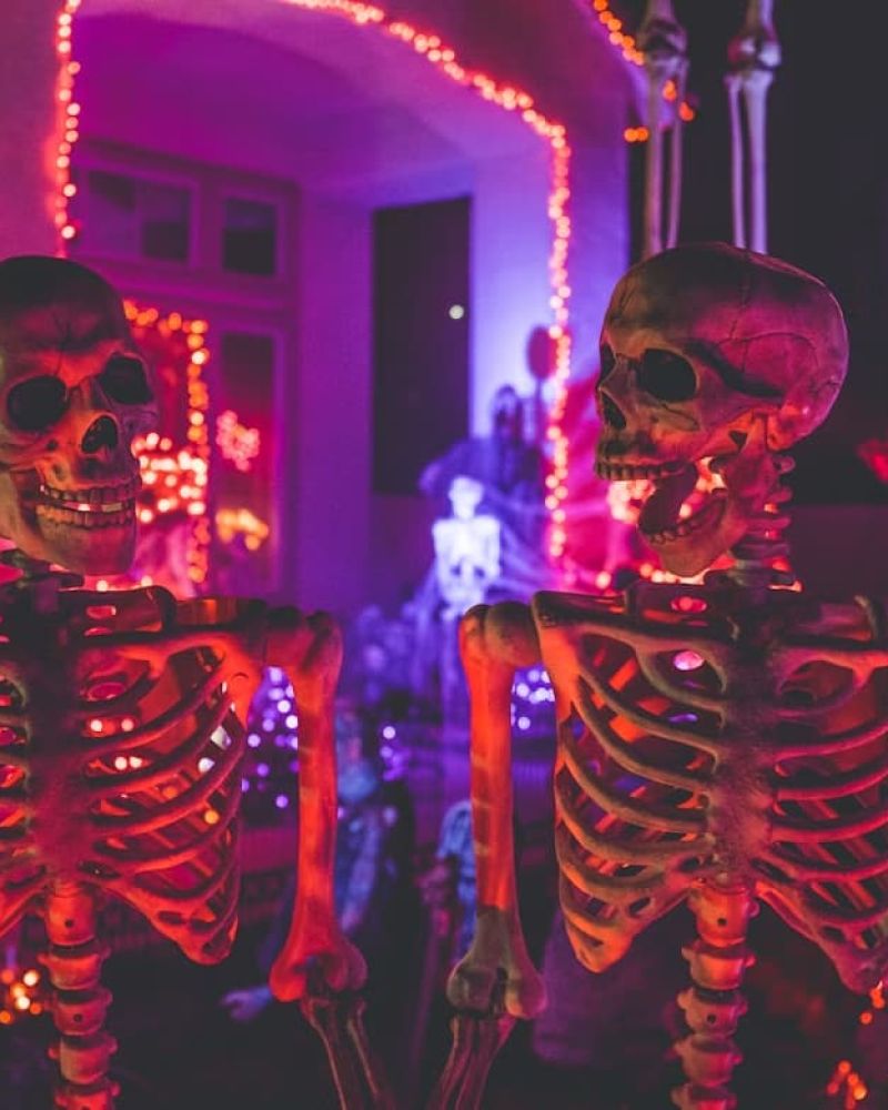 Skeleton Halloween decorations lit by red and purple lights on a porch