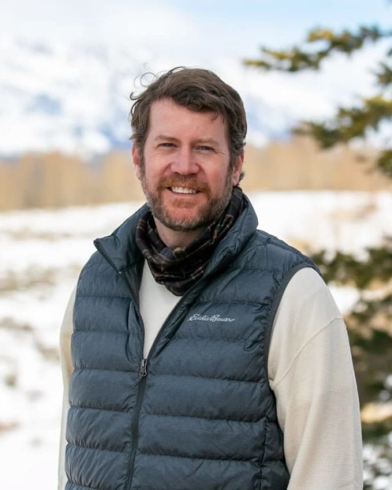 Bearded man in gray Eddie Bauer vest smiling in a snowy mountain landscape
