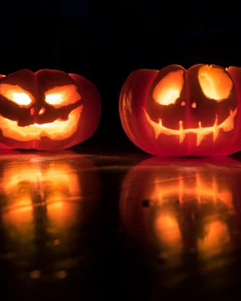 Two carved jack-o-lanterns glowing on a dark reflective surface