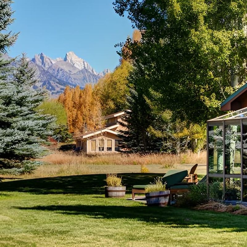 Log cabin with sunroom on a grassy lawn with Teton peaks in the distance