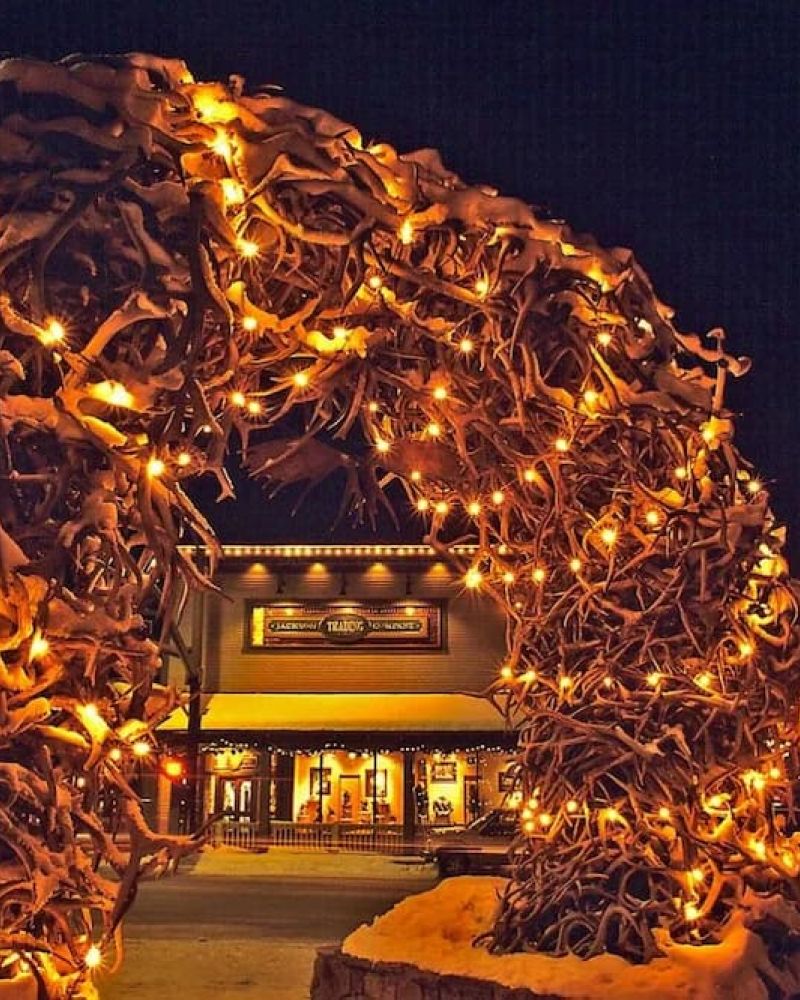 Snow-covered antler arch lit with string lights at night beside the Cowboy Bar